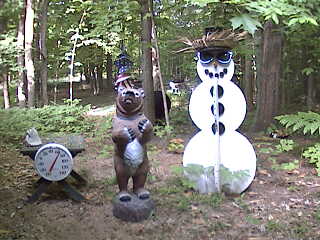 A real black bear is in the background between the snowman and the fake bear. Can you see it?